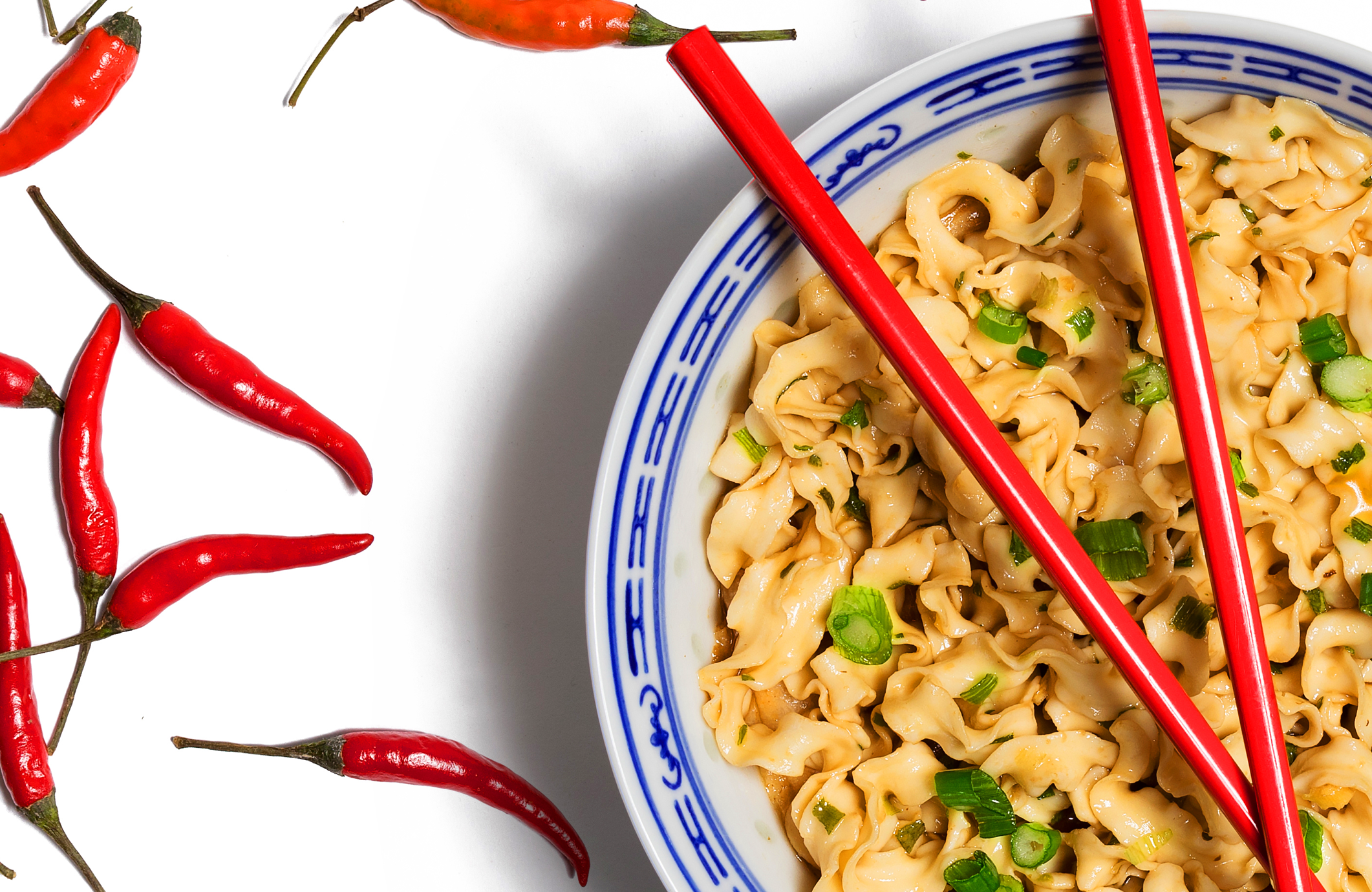 A bowl of A-Sha noodles with red chopsticks and red peppers